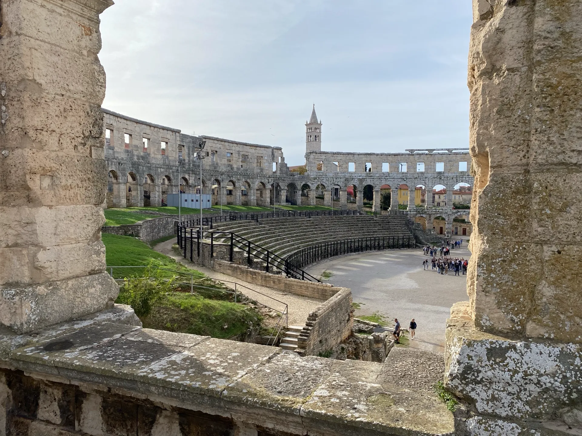 Stone seating and city view through the arches of Pula Arena